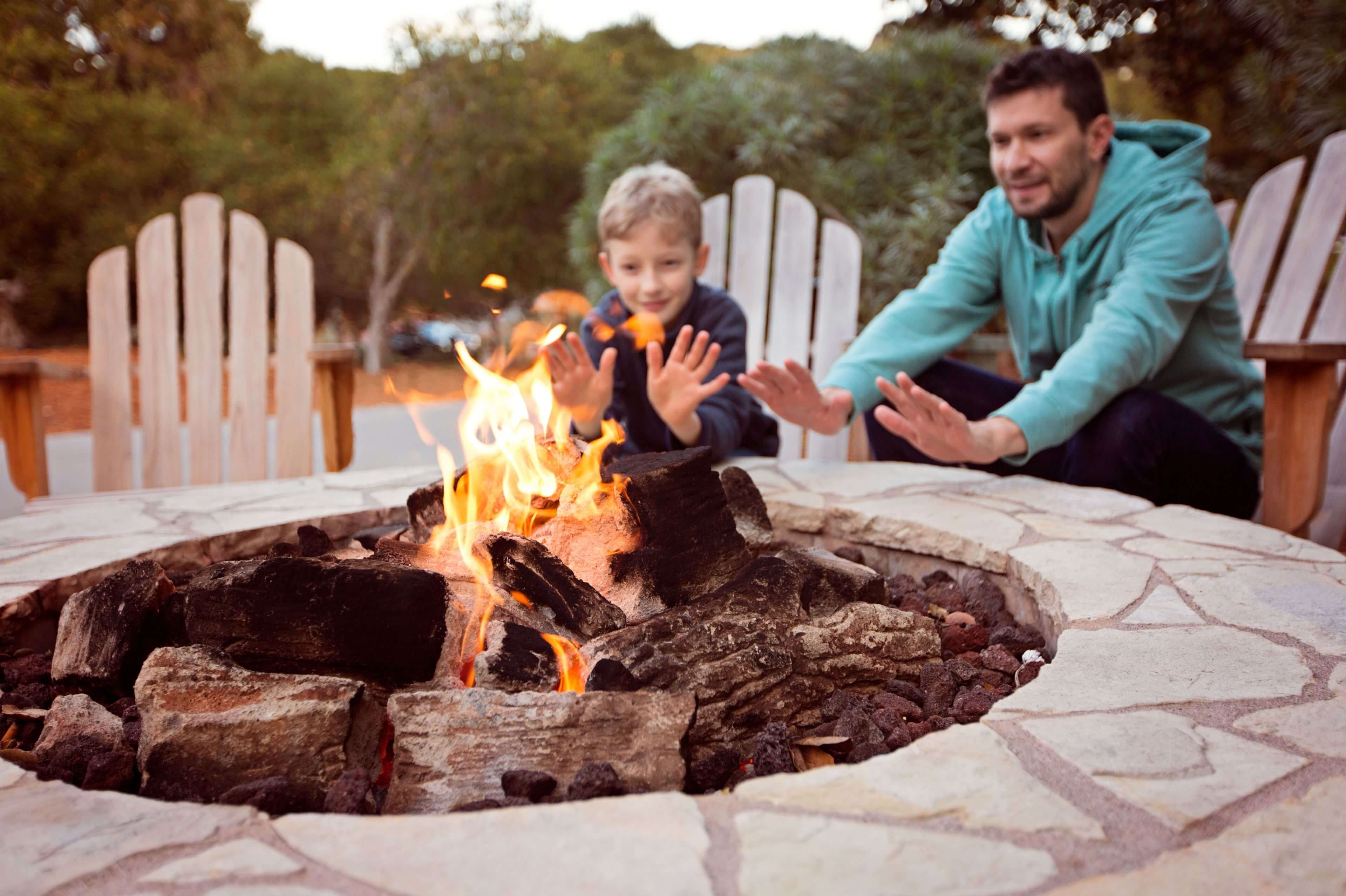 Father and son around outdoor fire pit with hands outstretched to warm up
