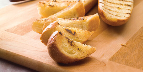 D’Italiano Garlic Baguette sliced into pieces pictured on a wooden cutting board
