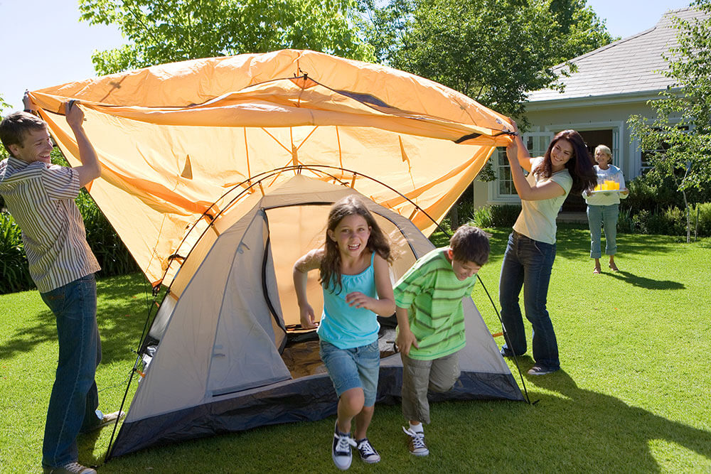 Un père fait du camping avec ses trois jeunes enfants dans sa cour. 